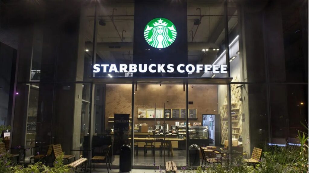 A Starbucks store viewed from the front at night with its lights and signs turned on.
