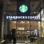 A Starbucks store viewed from the front at night with its lights and signs turned on.
