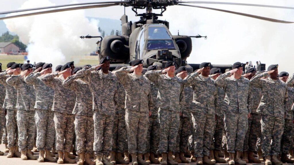 Many American soldiers saluting with their hands on their foreheads, with several military helicopters behind them.