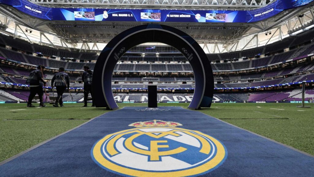 A panoramic view of Santiago Bernabéu Stadium with several Real Madrid crests all around.