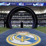A panoramic view of Santiago Bernabéu Stadium with several Real Madrid crests all around.
