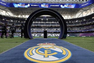 A panoramic view of Santiago Bernabéu Stadium with several Real Madrid crests all around.