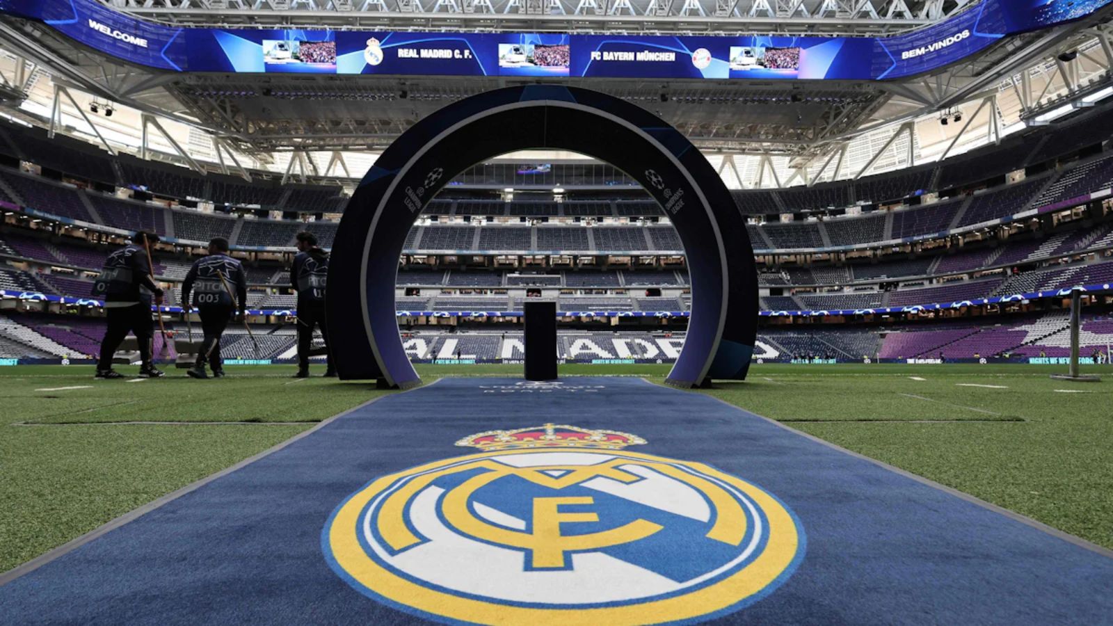 A panoramic view of Santiago Bernabéu Stadium with several Real Madrid crests all around.