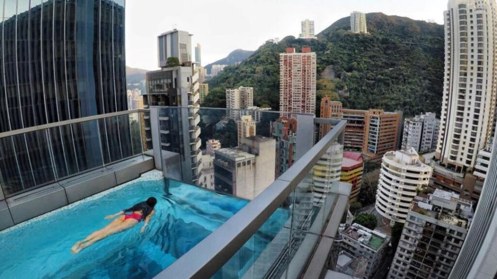 A famous building in Hong Kong with a swimming pool on one of its highest floors while a young woman swims in it.