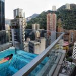 A famous building in Hong Kong with a swimming pool on one of its highest floors while a young woman swims in it.