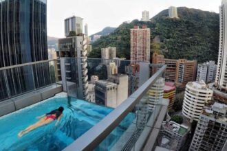 A famous building in Hong Kong with a swimming pool on one of its highest floors while a young woman swims in it.