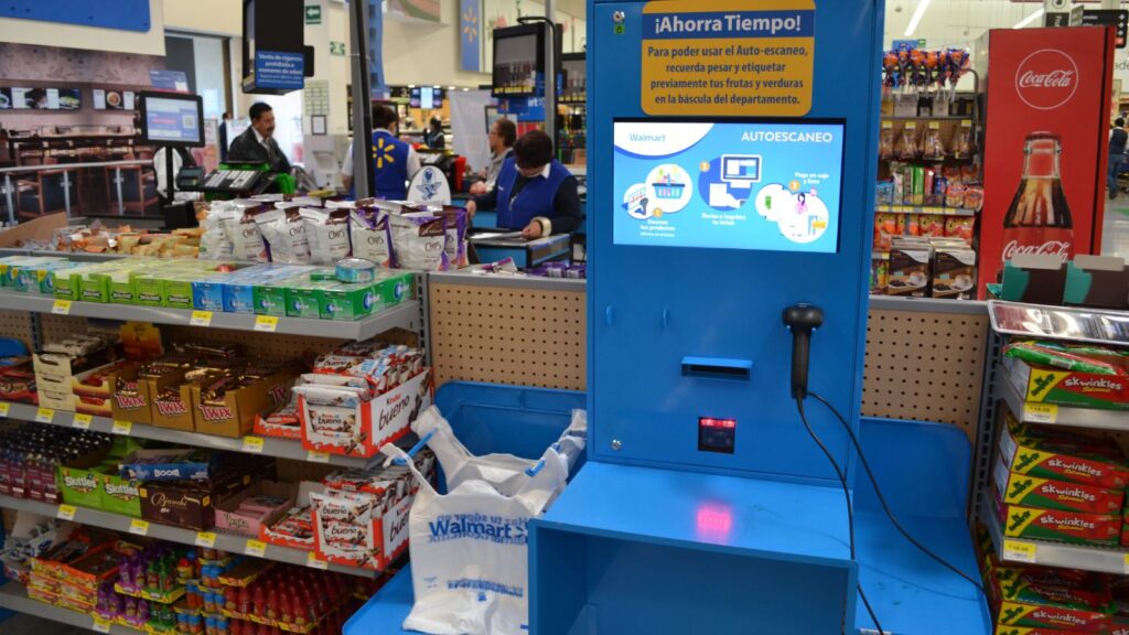 A blue and yellow self-checkout machine in the middle of a store.
