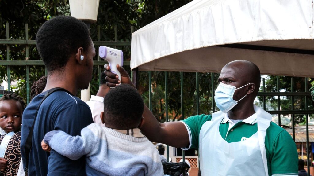 A man taking another person’s temperature while the person holds his child in his arms.