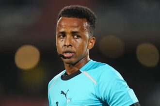 The African referee in the middle of a match wearing a blue uniform