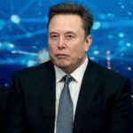 Elon Musk wearing a sharp suit while speaking at a press conference