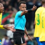 The Somali referee blowing the whistle for a foul against a team in yellow, whose players are protesting his decision