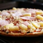 A frozen Hawaiian pizza being placed into an oven for baking