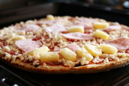 A frozen Hawaiian pizza being placed into an oven for baking