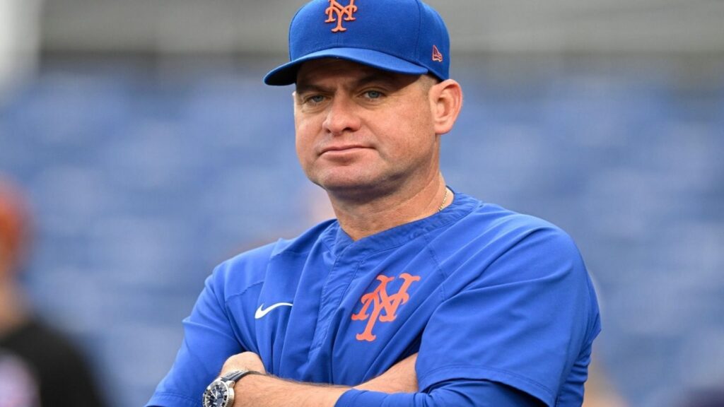 The now-former Mets manager sitting in his team's dugout, watching the game with a disappointed expression
