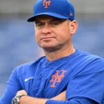 The now-former Mets manager sitting in his team's dugout, watching the game with a disappointed expression
