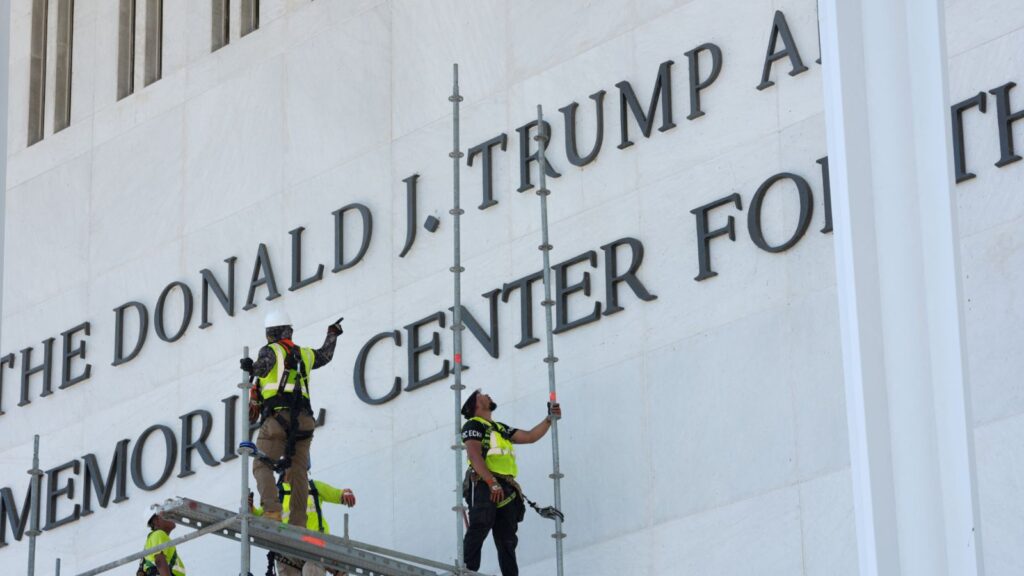 Workers removing Trump's name from a large wall