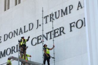 Workers removing Trump's name from a large wall