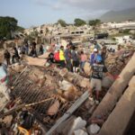 Several rescue workers standing on top of the rubble of a collapsed building while searching for survivors