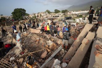 Several rescue workers standing on top of the rubble of a collapsed building while searching for survivors