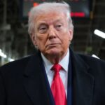 Donald Trump wearing an elegant suit while walking through a manufacturing facility