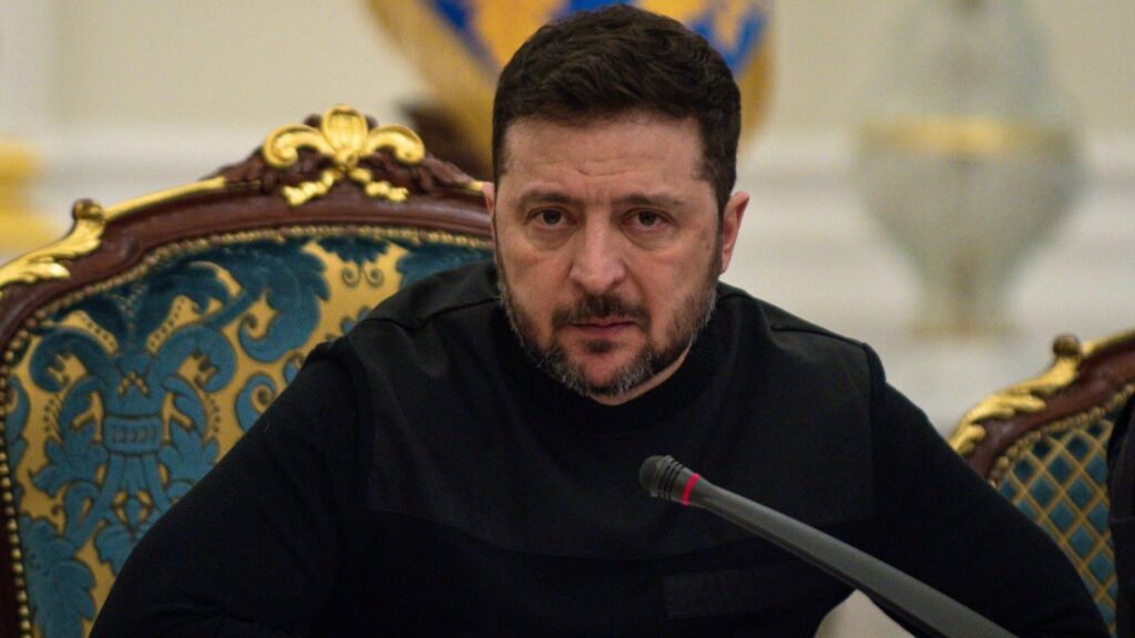 The leader of Ukraine sitting on an ornate chair, looking at the camera in front of several journalists