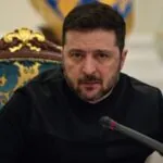 The leader of Ukraine sitting on an ornate chair, looking at the camera in front of several journalists