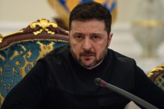 The leader of Ukraine sitting on an ornate chair, looking at the camera in front of several journalists