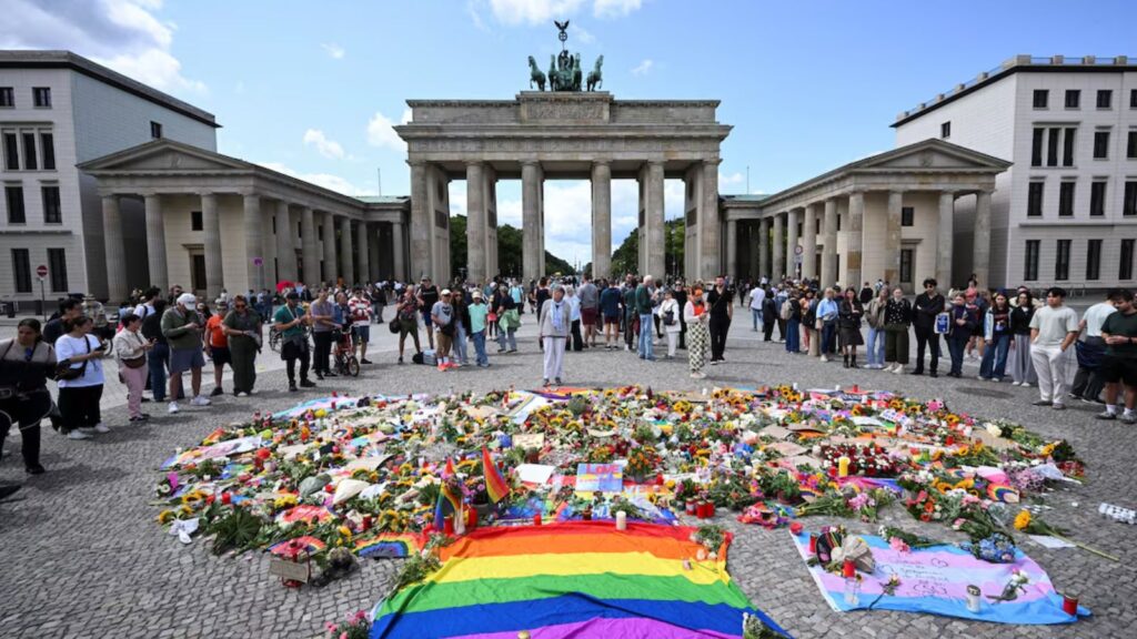 Several LGBTQ+ Pride participants surrounded by flowers and flags placed at the site of the attack in honor of the victims