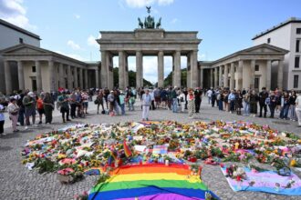 Several LGBTQ+ Pride participants surrounded by flowers and flags placed at the site of the attack in honor of the victims