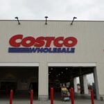 A Costco store viewed from the front, with several customers walking outside while pushing shopping carts