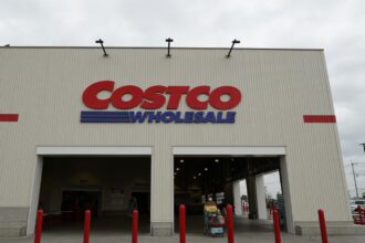 A Costco store viewed from the front, with several customers walking outside while pushing shopping carts