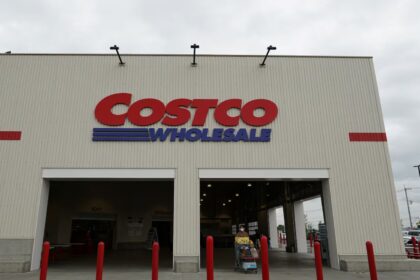 A Costco store viewed from the front, with several customers walking outside while pushing shopping carts