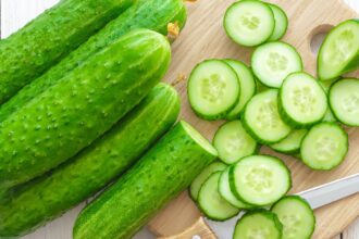 Several cucumbers stacked on a table, with one cucumber sliced into pieces beside them and a knife placed nearby