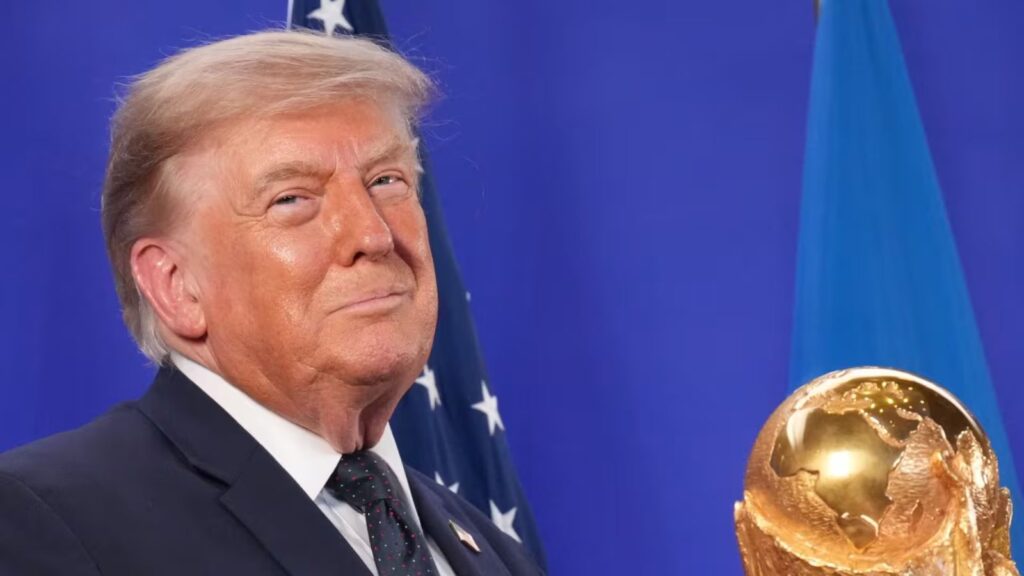 Donald Trump holding the World Cup trophy while smiling in front of the cameras