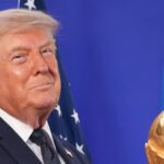 Donald Trump holding the World Cup trophy while smiling in front of the cameras