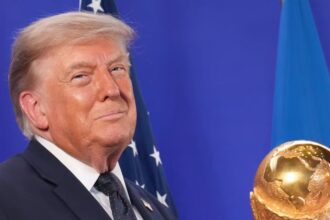 Donald Trump holding the World Cup trophy while smiling in front of the cameras