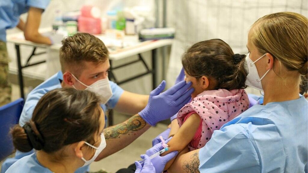Two nurses providing medical care to a young child while being held by his mother