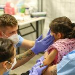 Two nurses providing medical care to a young child while being held by his mother