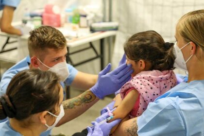 Two nurses providing medical care to a young child while being held by his mother