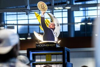 A cardboard cutout of Trump holding a Bitcoin coin high in the air