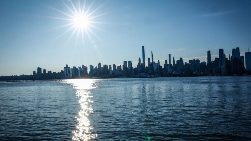 A panoramic view of the New York City skyline with the sun shining directly on it.