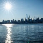 A panoramic view of the New York City skyline with the sun shining directly on it.