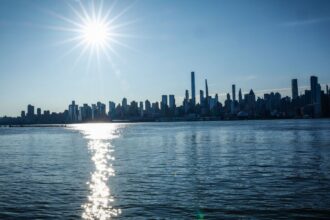 A panoramic view of the New York City skyline with the sun shining directly on it.