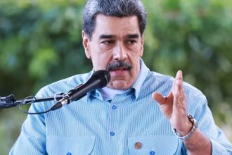 The former president of Venezuela speaking into a microphone while wearing a blue shirt with white checkered patterns
