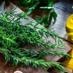 Rosemary the natural herb that could improve digestion and help your body better process protein A large sprig of rosemary placed on a wooden kitchen cutting board, with a bottle of rosemary oil beside the sprig