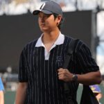 Ohtani walks toward the clubhouse wearing a black shirt with white stripes and a black cap