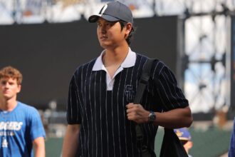 Ohtani walks toward the clubhouse wearing a black shirt with white stripes and a black cap