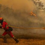 Several firefighters running while holding a hose to extinguish a wildfire