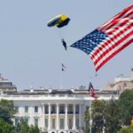 A man waving the United States flag while flying in a helicopter