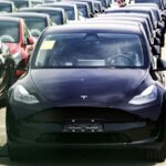 Several Tesla vehicles lined up in rows and covered to protect them from the sun